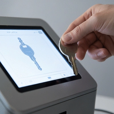 Close-up of a modern key being inserted into an electronic key duplication machine, with digital screen showing key profile, no text, no words, no typography, clean image